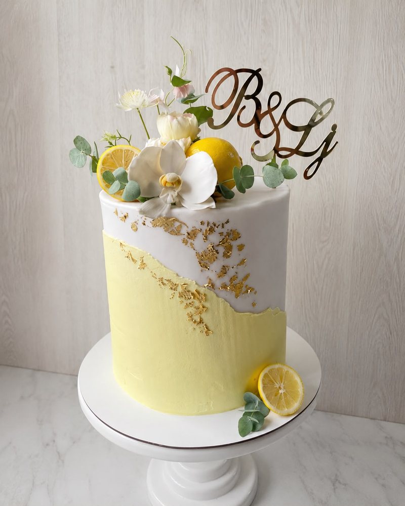 Žuta torta sa limunima, bijelim cvijećem i zlatnim detaljima.